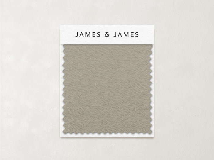 The Beige - Leather Swatch by James+James features a subtle, pebbled texture and zigzag-cut edges in muted taupe. Ideal for relaxed interiors, this soft Ultra Leather sample is labeled with the James+James brand at the top.