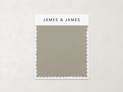 The Beige - Leather Swatch by James+James features a subtle, pebbled texture and zigzag-cut edges in muted taupe. Ideal for relaxed interiors, this soft Ultra Leather sample is labeled with the James+James brand at the top.