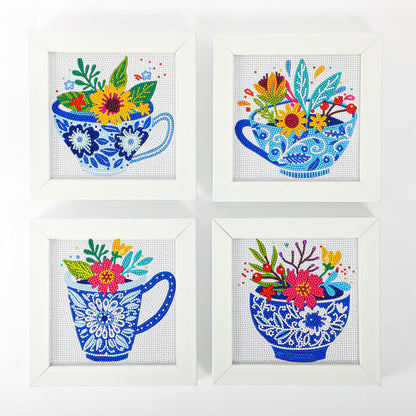 Four white-framed Diamond Dotz Mini Dotz artworks display blue teacups with intricate floral patterns, each brimming with colorful flowers and leaves, arranged in a two-by-two grid on a white background.