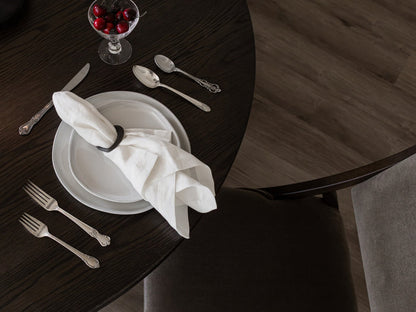 A dark wood dining table set with a white plate, napkin, silverware, and glass bowl of cherries is viewed from above. Beside the table, a James+James Mink - Mohair Swatch chair adds an inviting, layered touch.